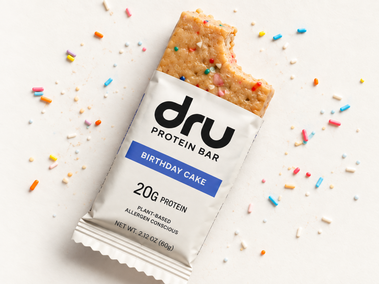 Opened DRU Birthday Cake protein bar with a bite taken out, surrounded by sprinkles